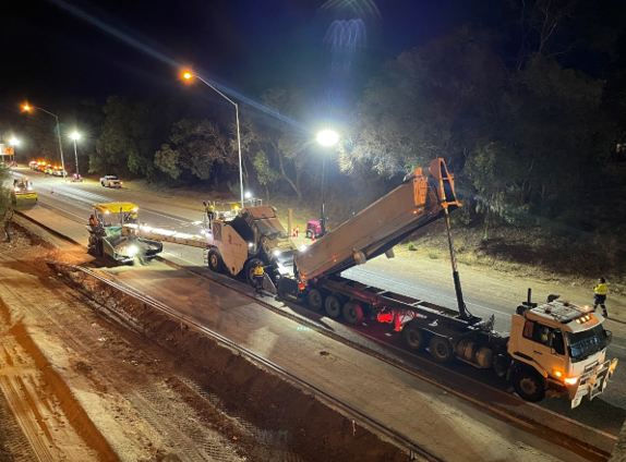 SuperCivil crew carrying out night road maintenance works under floodlights, with a road profiler and low-loader truck resurfacing a highway in Western Australia