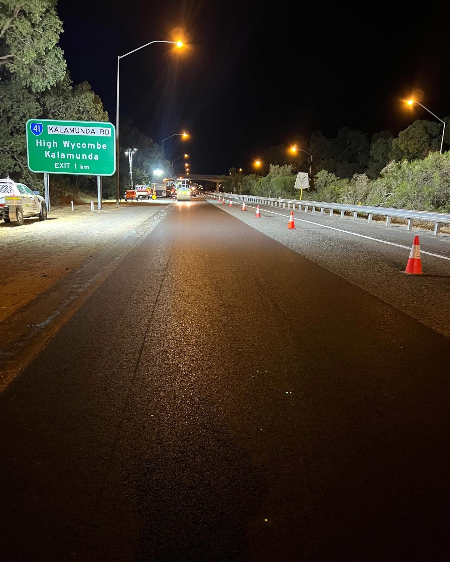 Night-time freeway resurfacing near the Kalamunda Road exit in Western Australia with roller, crew and traffic management