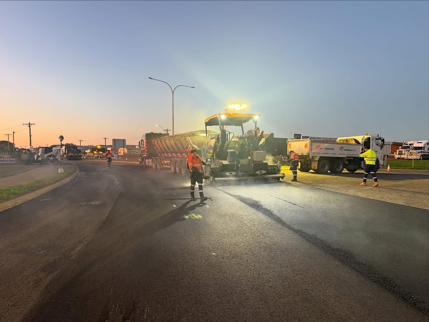 SuperCivil crew and asphalt paver laying fresh asphalt on a wide regional Western Australian road at dusk
