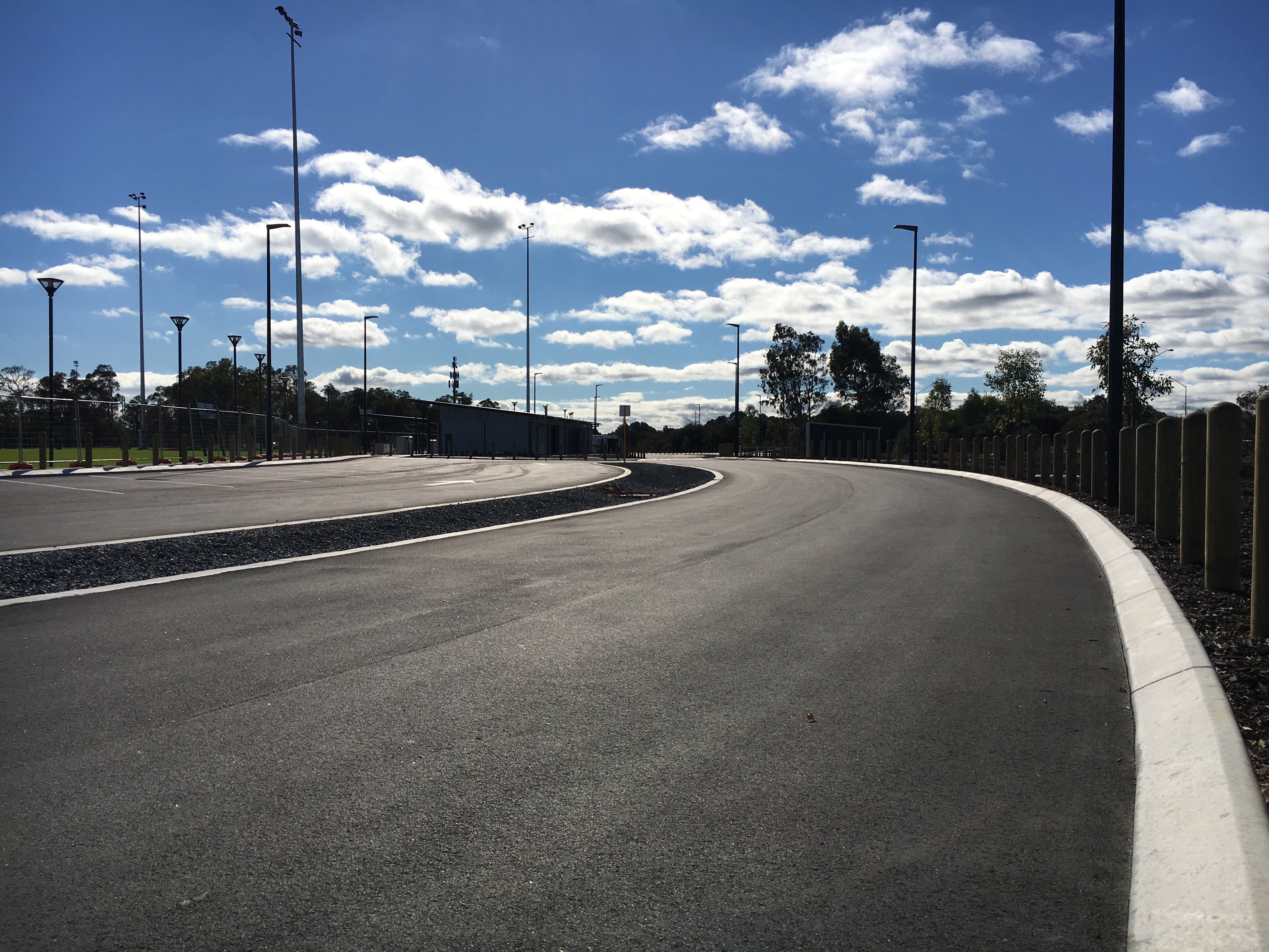 SuperCivil freshly laid asphalt access road with white concrete kerbing sweeping through a Western Australian sports complex under a blue sky