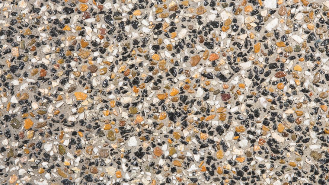Close-up of a polished exposed aggregate concrete finish showing black, tan, orange and cream stones set in cement