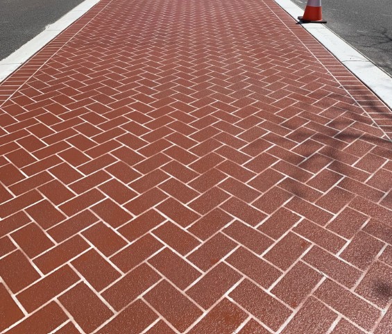 Red herringbone brick-pattern faux paving finish on a concrete footpath bordered by white edging on a Western Australian project