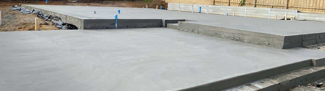 Freshly poured and finished grey concrete house slab with stepped split-level sections and plumbing penetrations on a Western Australian residential building site