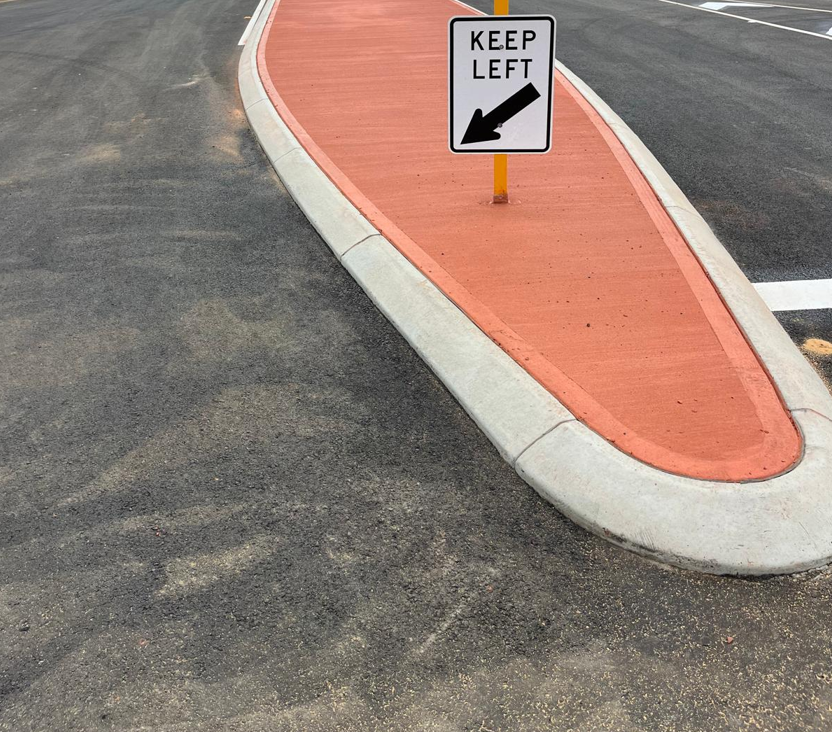 Completed traffic island with grey concrete kerbing and red coloured concrete infill topped with a KEEP LEFT sign on a Western Australian road upgrade