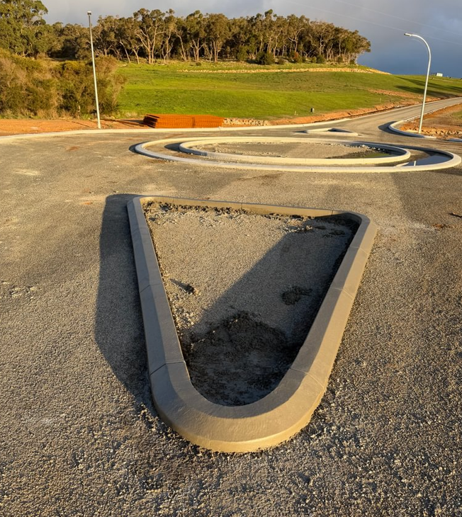 Freshly extruded continuous concrete kerbing forming a teardrop traffic island and circular island on a newly built regional Western Australian road