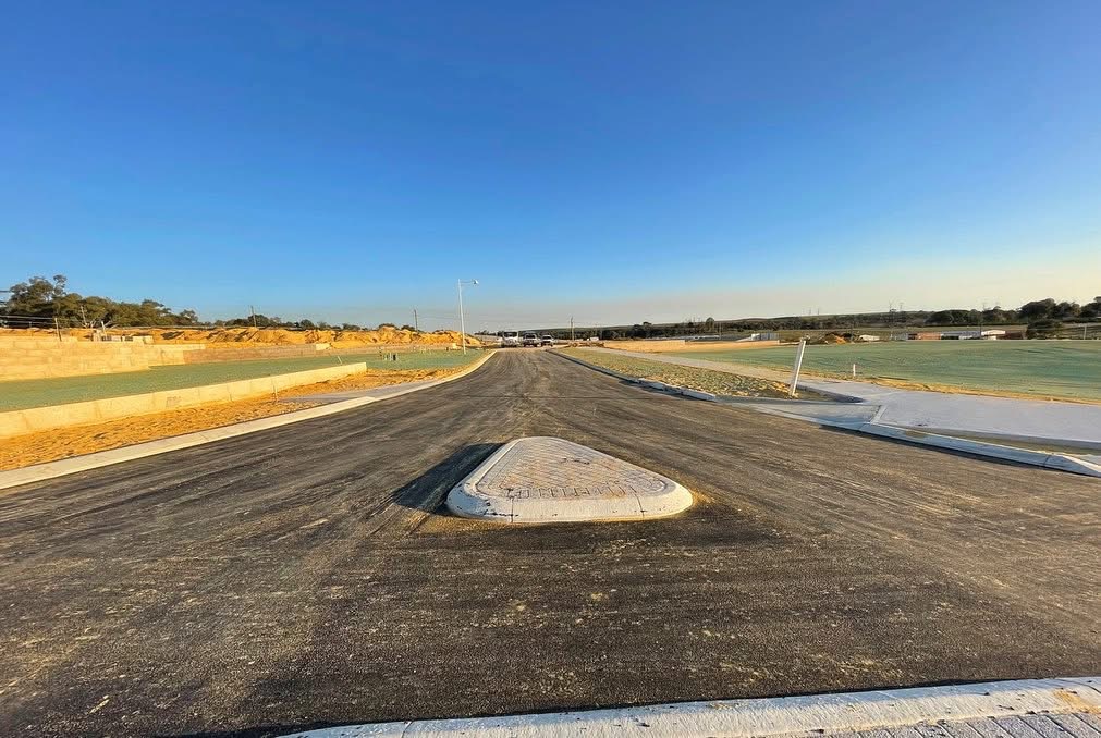 Newly constructed subdivision road with fresh asphalt, a raised concrete median island and concrete kerbing lining both edges on a SuperCivil civil works project in Western Australia