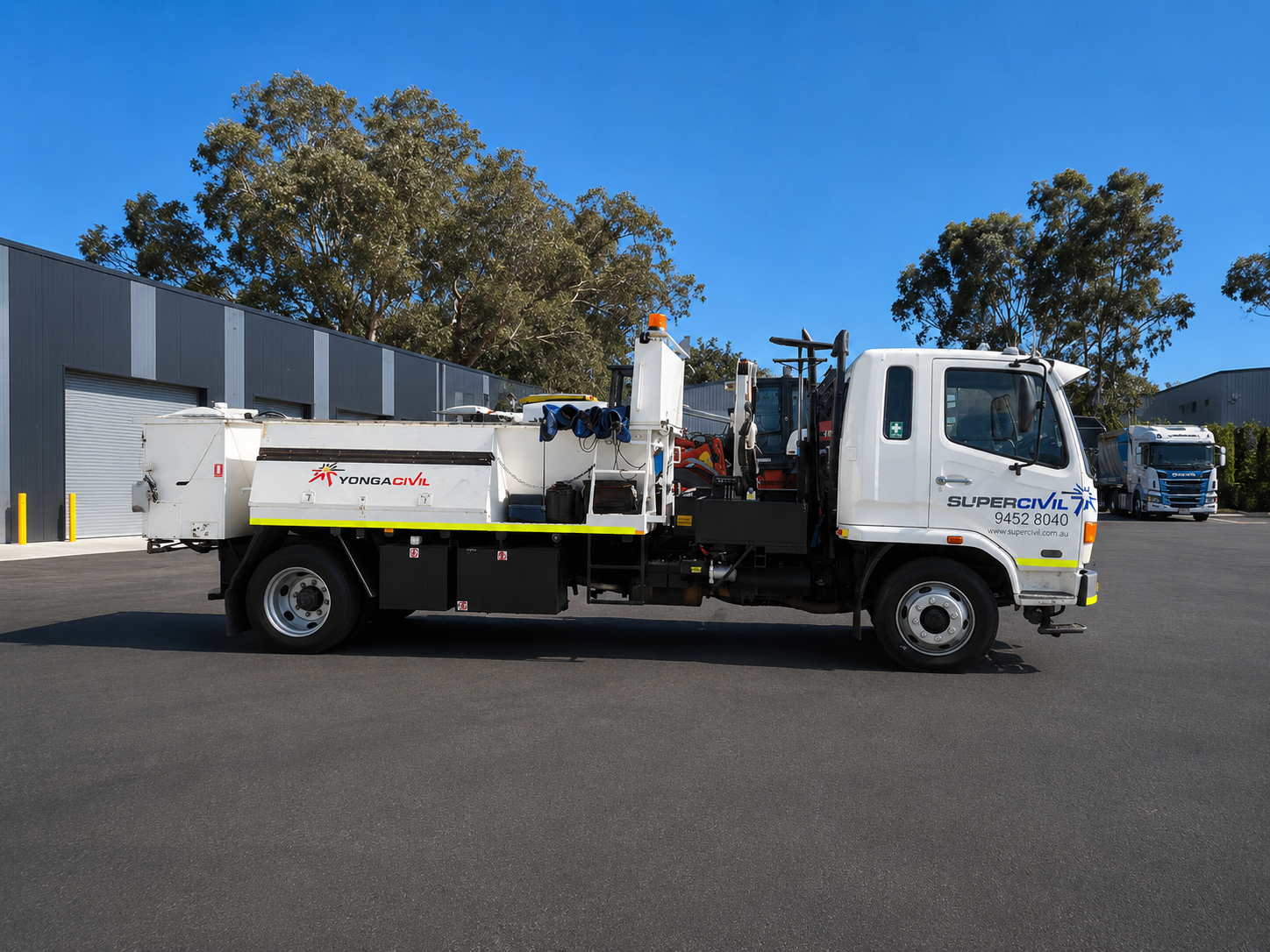 White SuperCivil Hino flocon maintenance truck fitted with road maintenance equipment, parked outside an industrial warehouse under a clear blue sky in Western Australia