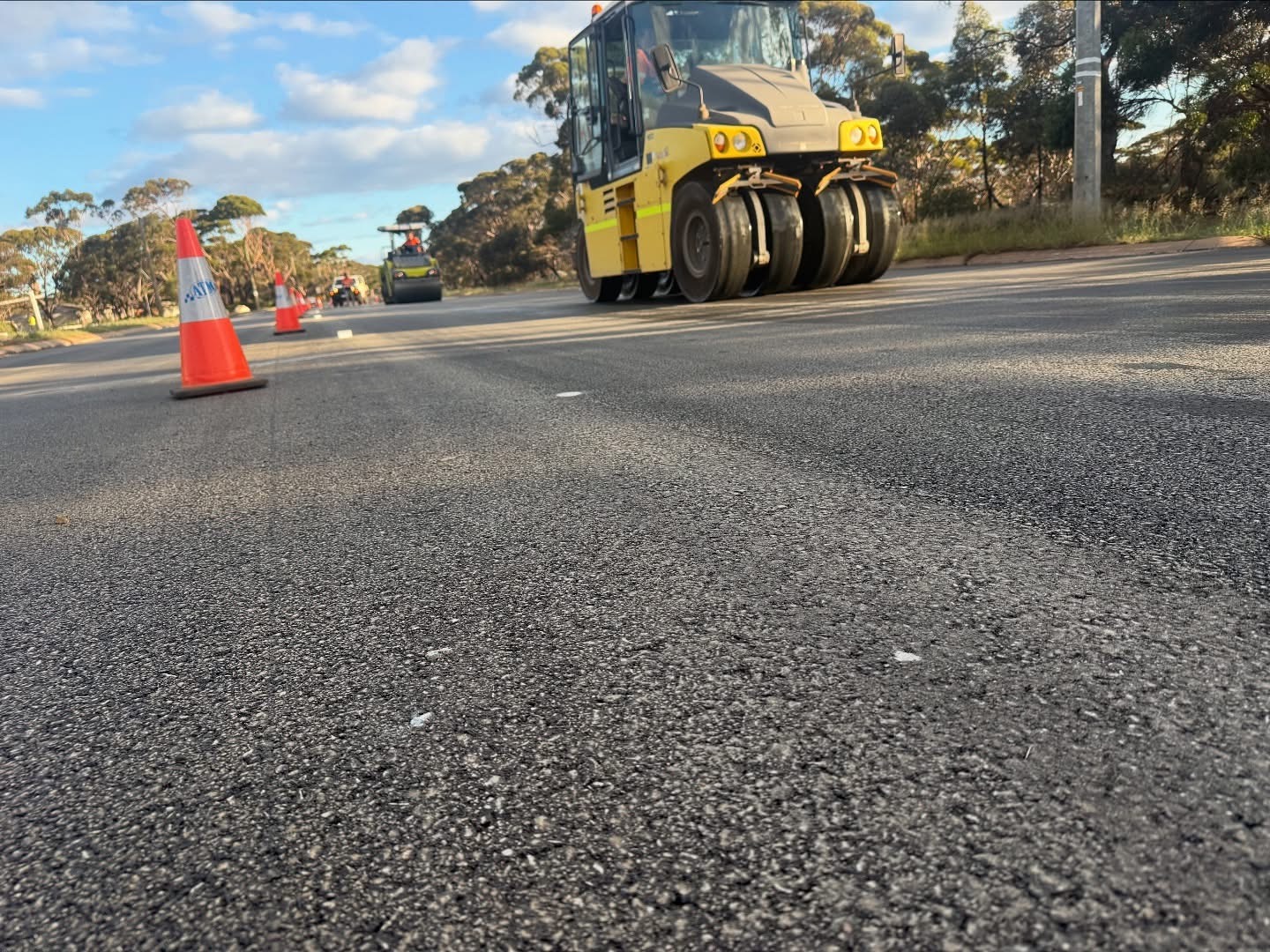 SuperCivil multi-tyred pneumatic roller compacting a freshly sprayed and aggregated road seal on a regional Western Australian road, with traffic cones and hi-vis crew